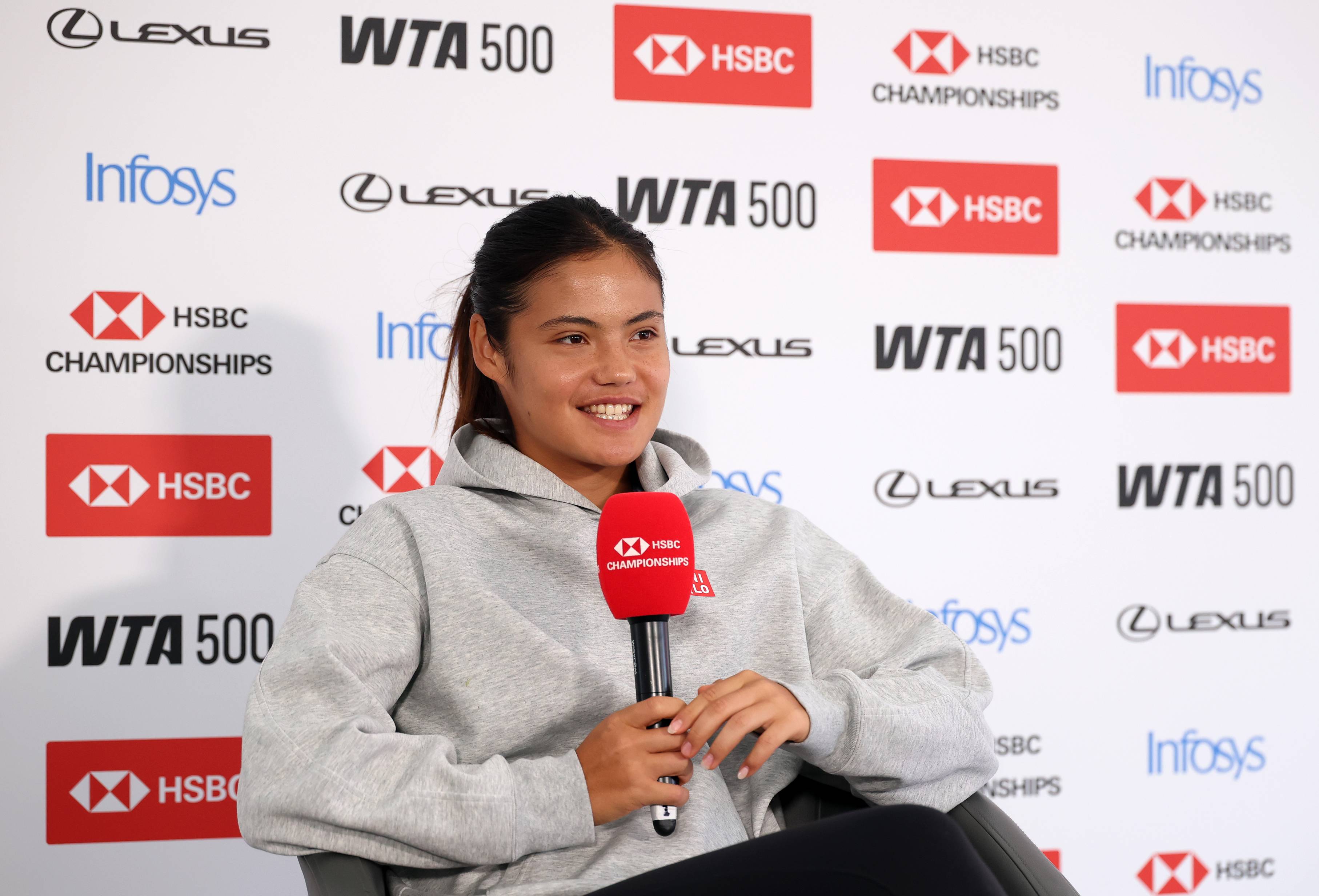 Emma Raducanu smiling while holding a microphone during a press conference at the HSBC Championships