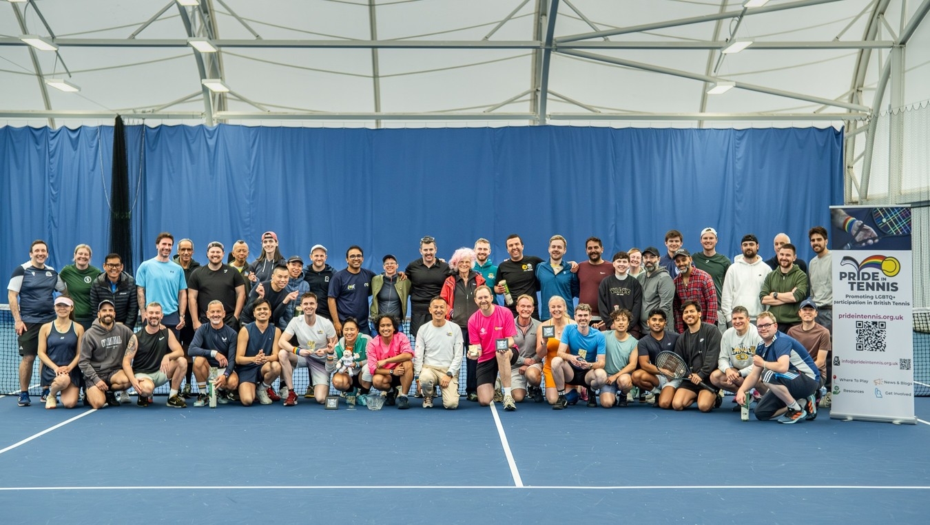 A large group of people pose for a photo on a blue indoor tennis court