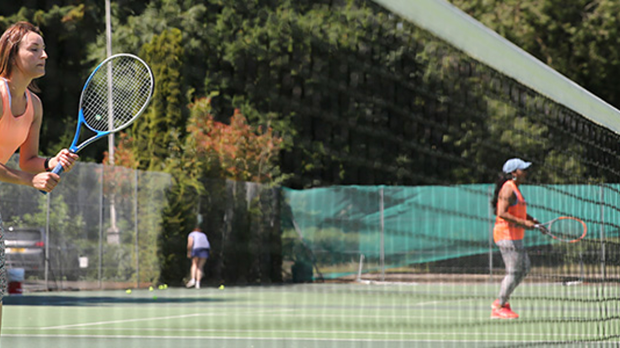 Four adults playing tennis with one getting ready to volley by the net