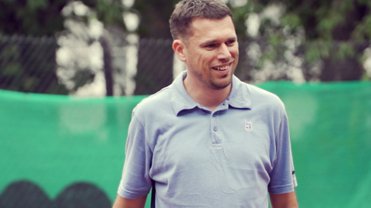 Steve mccann standing on a tennis court wearing a blue shirt and smiling 
