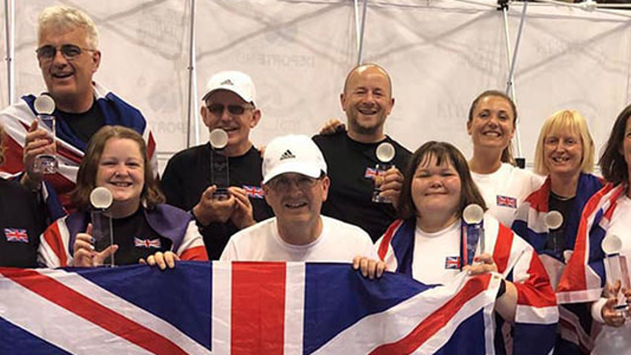 GB players holding winning trophies in hand and four of the players holding a large GB flag at the front