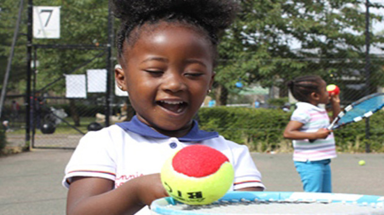 A small child with a tennis ball balancing on her racket