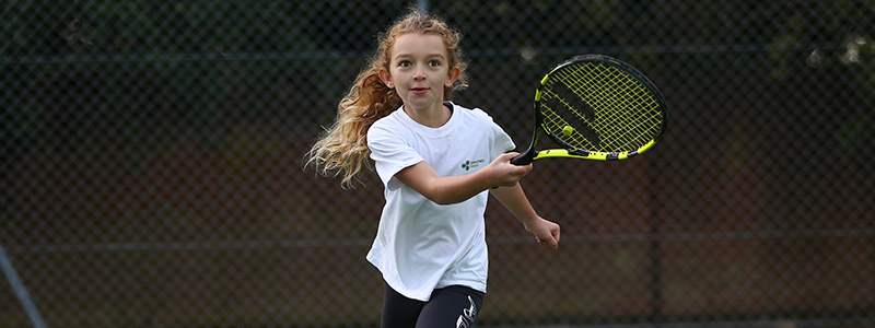 Young girl playing tennis with a black and yellow racket