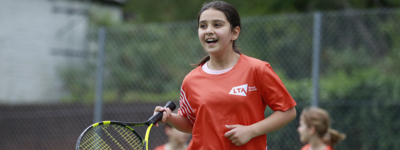 junior player on courting holding racket wearing a red LTA tennis top