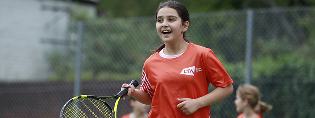 junior player on courting holding racket wearing a red LTA tennis top