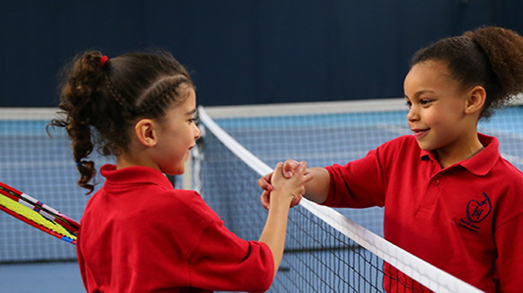 two kids wearing red tops shaking hands over net on tennis court