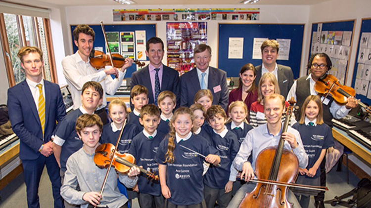 tim henman standing besides school kids in a classroom with few children holding violins at Reed’s School in Cobham, Surrey 