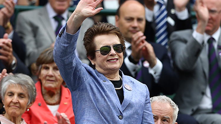 Billie Jean King standing up in a crowd waving and smiling