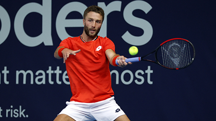 action shot of liam broady on court racket in air about to hit the ball
