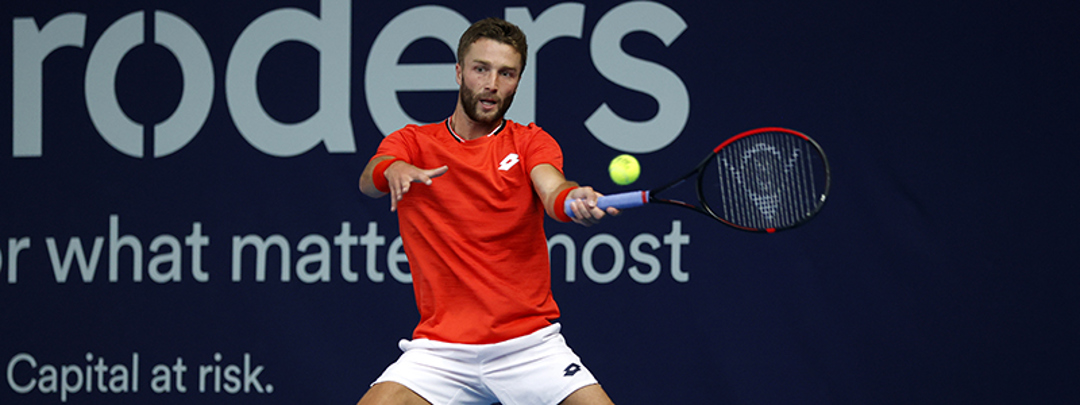 action shot of liam broady on court racket in air about to hit the ball