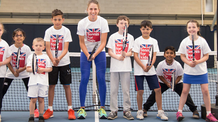 Johanna Konta with a group of children, all holding tennis rackets in front of a tennis net on a court
