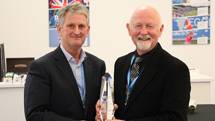 keith reynolds and coty in suits both holding one glass trophy between them