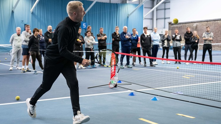 Male coach on mini tennis court demonstrating drill to crowd