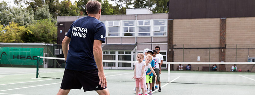 A coach coaching a group of young tennis students