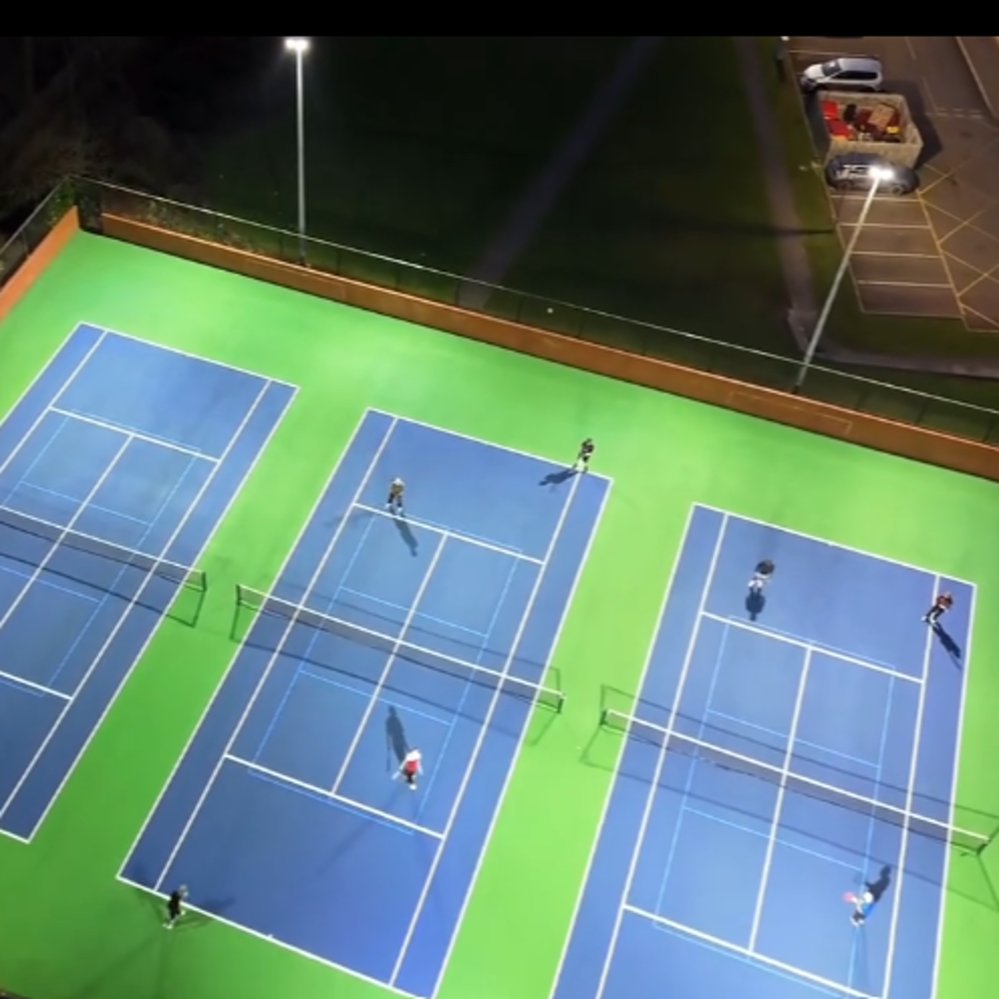 An aerial view of tennis courts lit up by floodlights